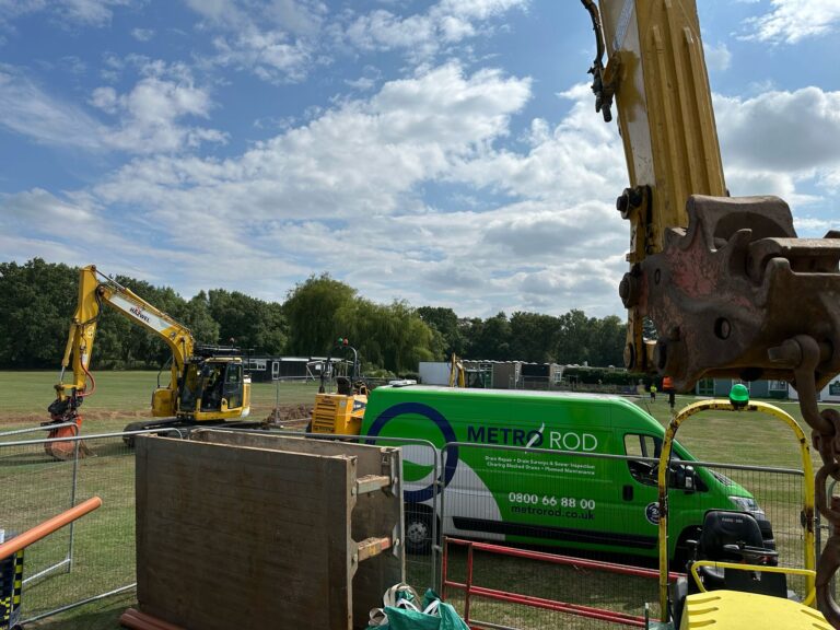 A picture of a Metro Rod van and excavators on a primary school field